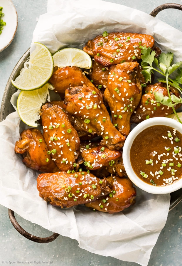 Overhead photo of Chinese Wings sprinkled with sesame seeds and a ramekin of Asian wing sauce in a paper-lined bowl. 