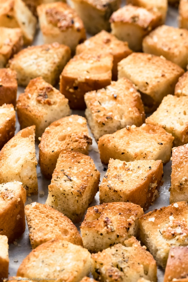Angled, up close photo of seasoned homemade croutons on a piece of parchment paper.