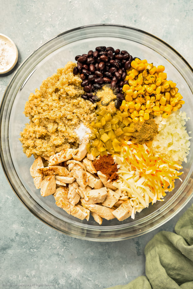 Overhead photo of a large glass bowl filled with shredded chicken, quinoa, black beans, corn, green chiles, onions, Mexican seasonings and shredded cheeses.