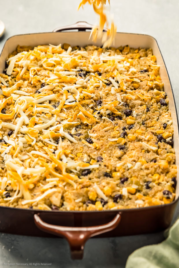 Angled photo of a hand sprinkling shredded Mexican cheese blend over a chicken quinoa casserole.
