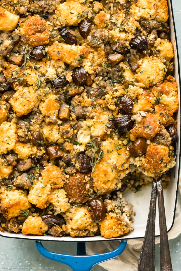 Overhead, close-up photo of Chestnut Cornbread Dressing in a blue baking dish with a serving of stuffing removed from the dish.
