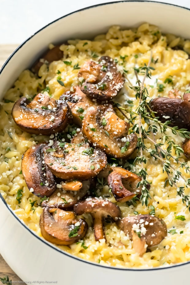 Angled, up-close photo of Mushroom Risotto garnished with fresh thyme and grated parmesan in a white saucepan.