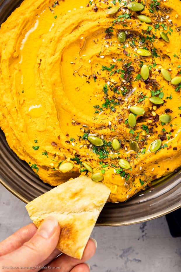 Overhead photo of a pita chip inserted into a bowl of freshly made sweet potato hummus recipe.