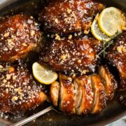 Overhead photo of baked chicken thighs with balsamic fig glaze and slices of lemon in a baking dish.