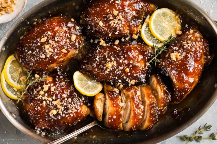Overhead photo of baked chicken thighs with balsamic fig glaze and slices of lemon in a baking dish.