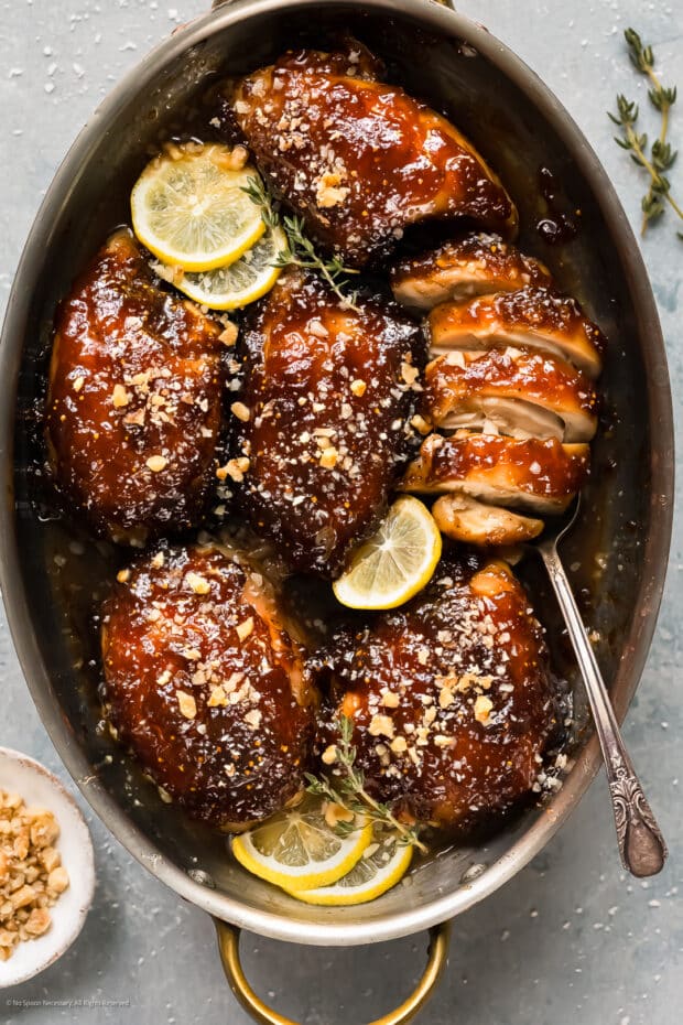 Overhead photo of six balsamic fig chicken thighs with garnished with lemon slices in a baking pan.