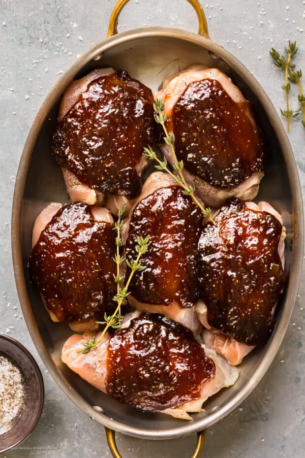 Overhead photo of six raw chicken thighs smothered with fig sauce in a baking dish.