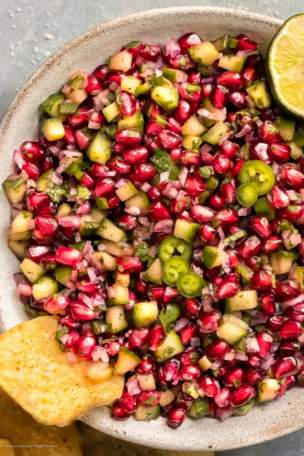 Overhead photo of pomegranate and cucumber salad in a bowl with a tortilla chip scooped into the salad.