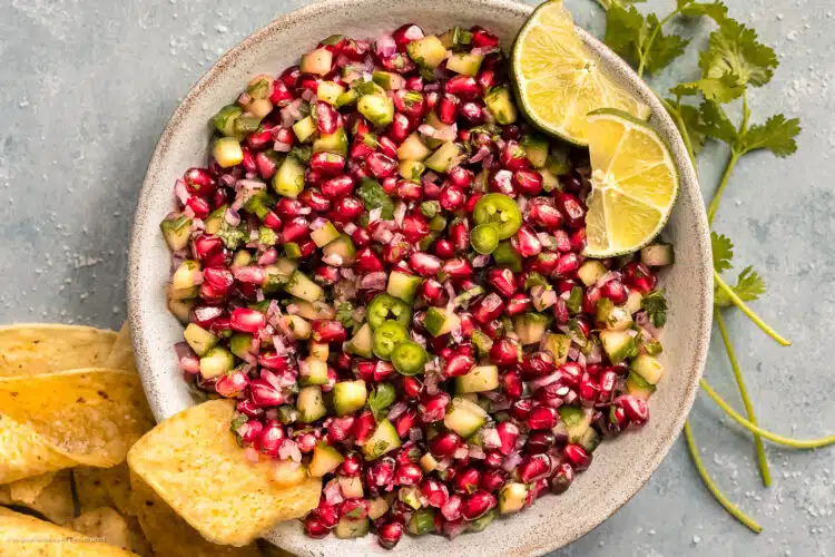 Overhead photo of pomegranate salsa in a serving bowl with tortilla chips next to the bowl.