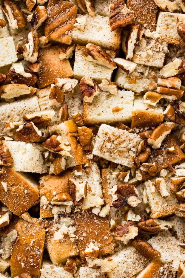Overhead, close-up photo of cubes of brioche bread sprinkled with cinnamon and chopped pecans - photo of the main ingredients in cinnamon baked French toast.