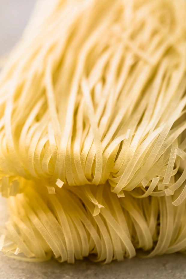 Angled, close-up photo of two stacks of dry Asian rice noodles (photo of one of the main ingredients in the recipe).