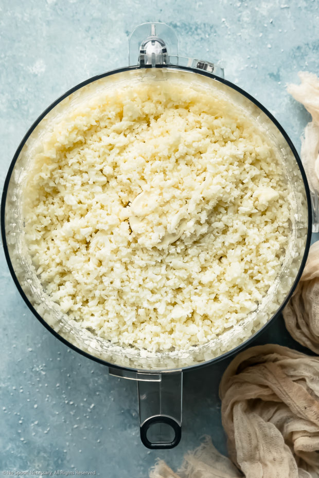 Overhead photo of riced cauliflower florets in the bowl of a food processor (photo of how to make cauliflower rice)..