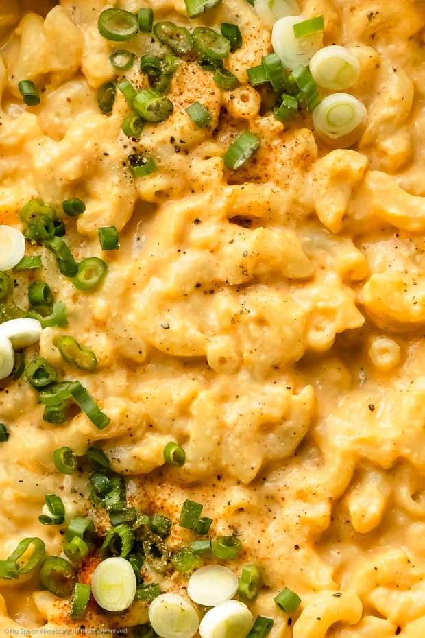 Overhead, close up photo of Healthy Macaroni and Cheese garnished with sliced scallions, paprika and fresh ground black pepper.