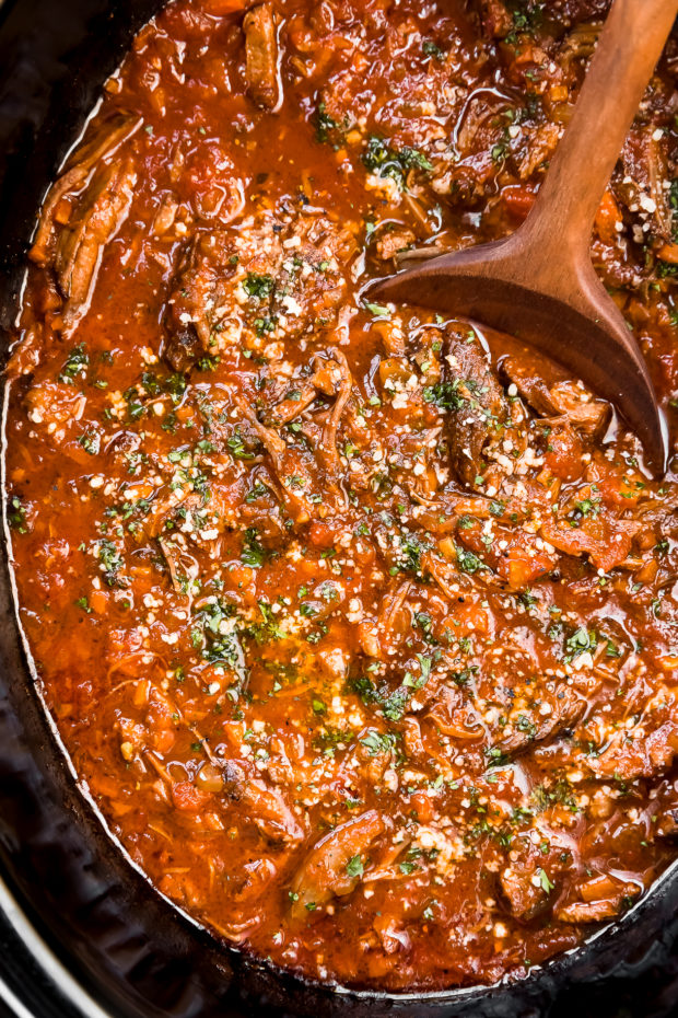 Overhead, close-up photo of fully cooked Short Rib Ragu Bolognese garnished with chopped parsley and grated parmesan in the pot of a slow cooker - photo of the final step of the recipe. 