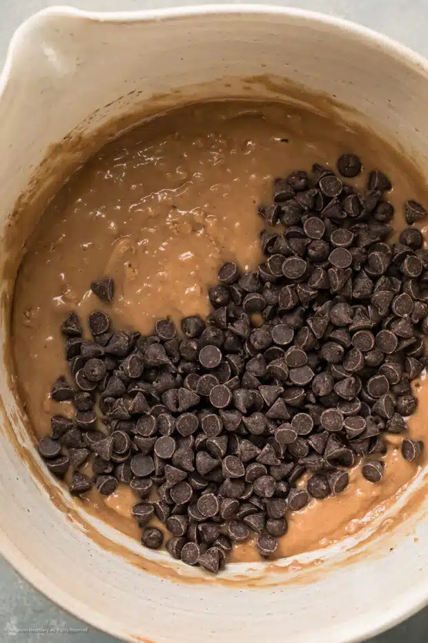 Overhead photo of raw chocolate coffee cake batter topped with chocolate chips in a large white mixing bowl.