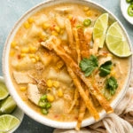 Overhead landscape photo of Chicken Corn Chowder topped with crispy tortilla strips and lime wedges in a white bowl with ramekins of sliced jalapenos and lime wedges next to the bowl.