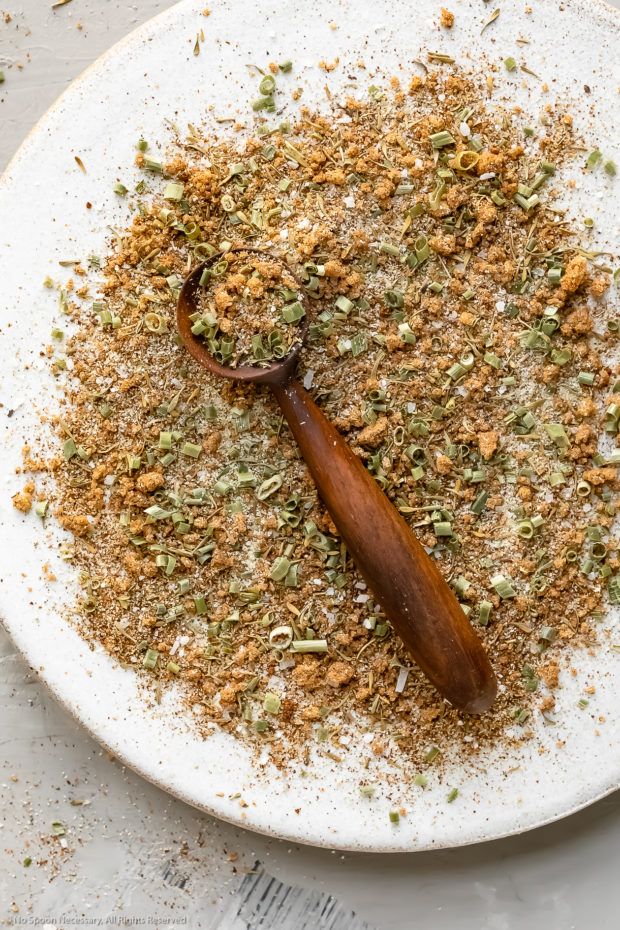 Overhead photo of Jamaican Jerk Spice Blend on a white plate with a small wooden spoon filled with the blend laying on top.