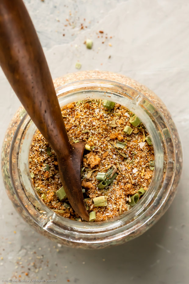 Overhead photo of Caribbean Jerk Seasoning in a small glass jar with a wooden spoon inserted into the spice blend.