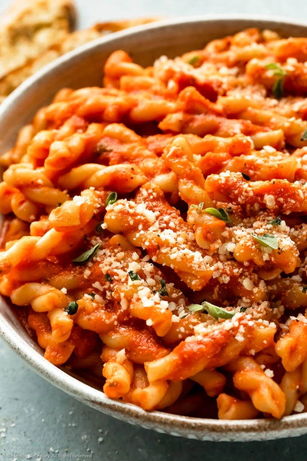 Angled, up-close photo of cooked gemelli pasta tossed with vodka sauce in a white bowl - photo of one way to use vodka sauce.