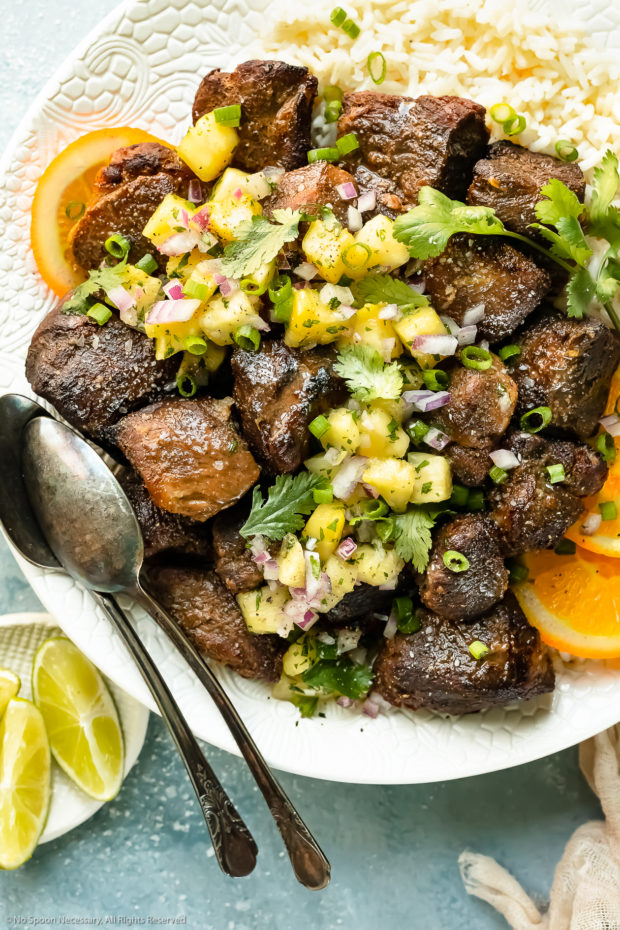 Overhead photo of a plate of Jamaican Jerk Pork topped with tropical salsa on a bed of white rice with orange slices; with a ramekin of lime wedges next to the plate.