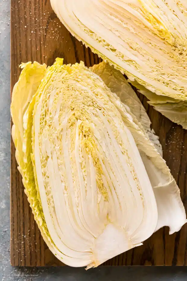 Overhead photo of a head of napa cabbage cut into half to expose the inside on a gray wood cutting board.