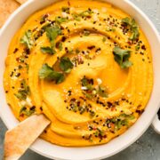 Overhead photo of a bowl of carrot hummus garnished with sesame seeds and cilantro