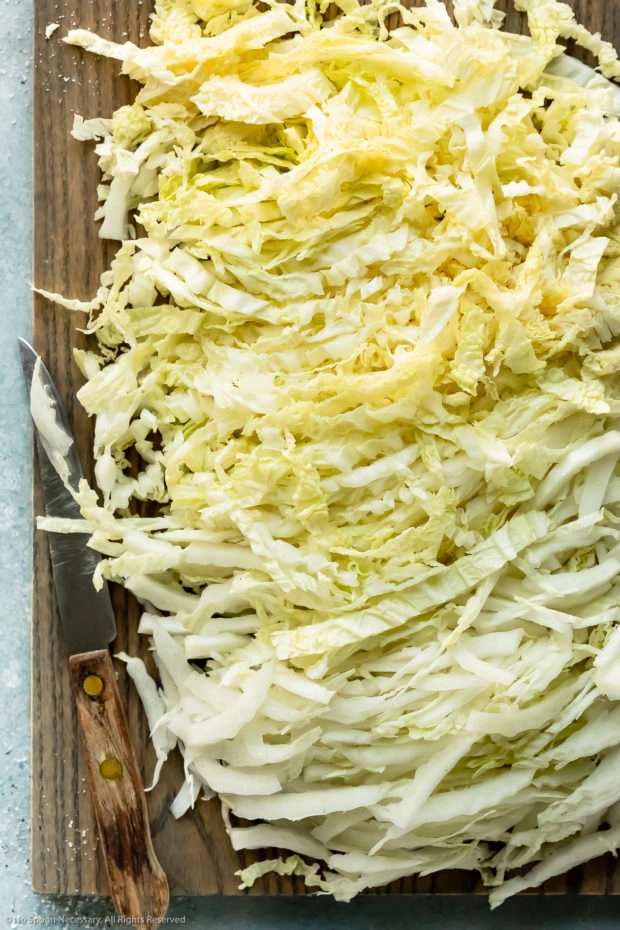 Overhead photo of shredded napa cabbage on a gray wood cutting board with a knife laying next to the cabbage