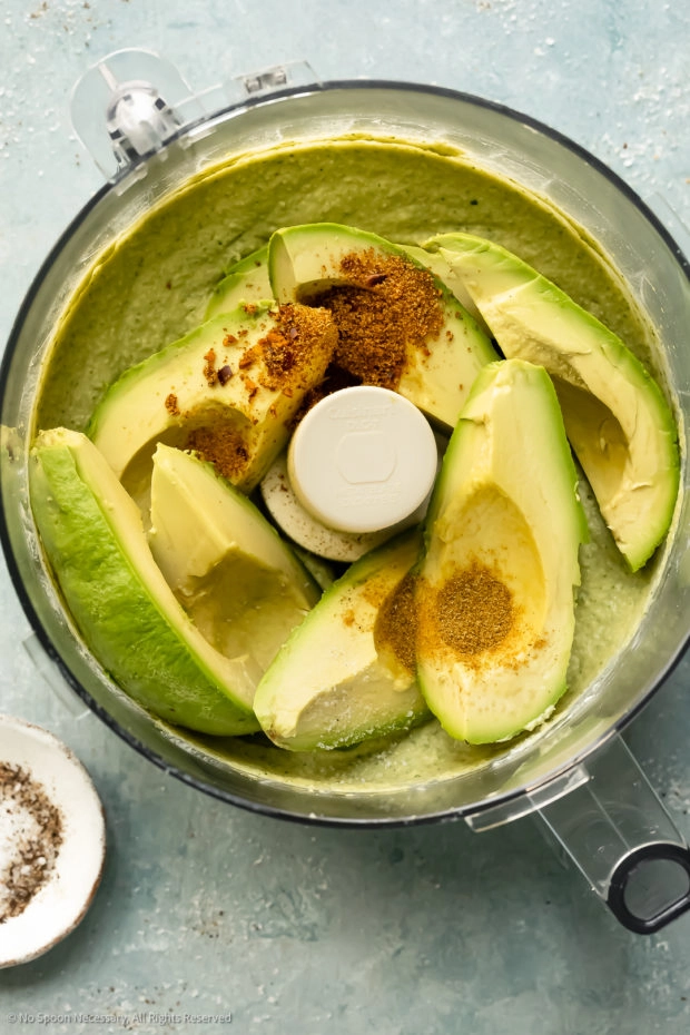 Overhead photo of a food processor bowl filled with creamy hummus and chunks of avocado. 