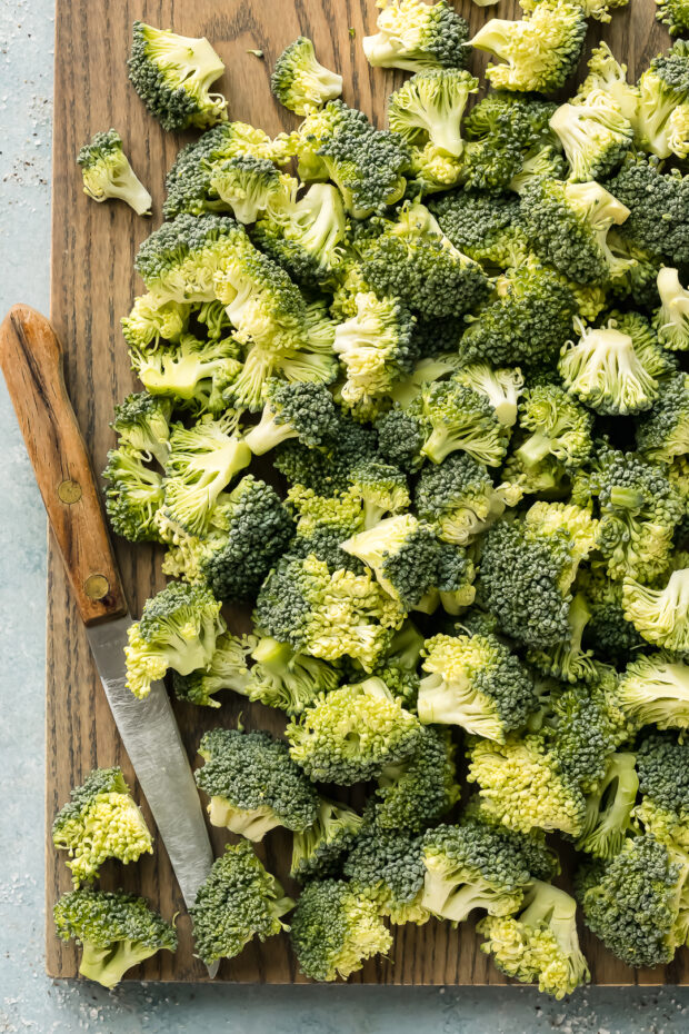 Overhead photo of raw broccoli florets for salad on a wood cutting board.