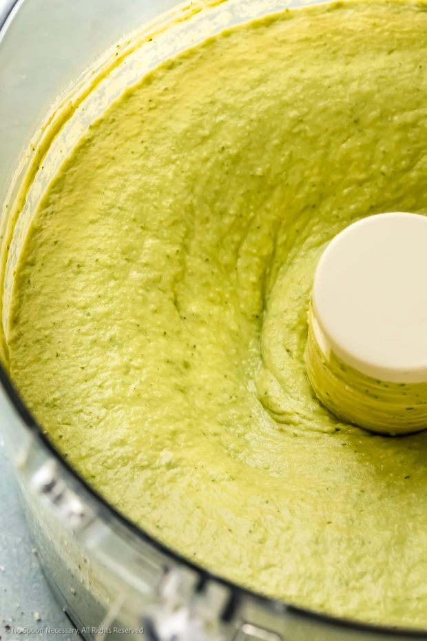 Angled close-up photo of spicy avocado hummus in a food processor bowl.