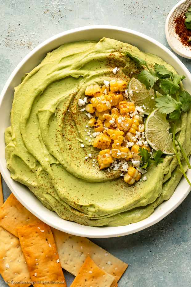 Overhead photo of spicy hummus made with avocado and sriracha and topped with grilled corn kernels. 