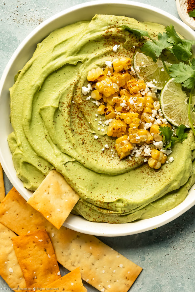 Overhead photo of a bowl of Spicy Avocado Hummus with a flatbread cracker inserted into the dip.