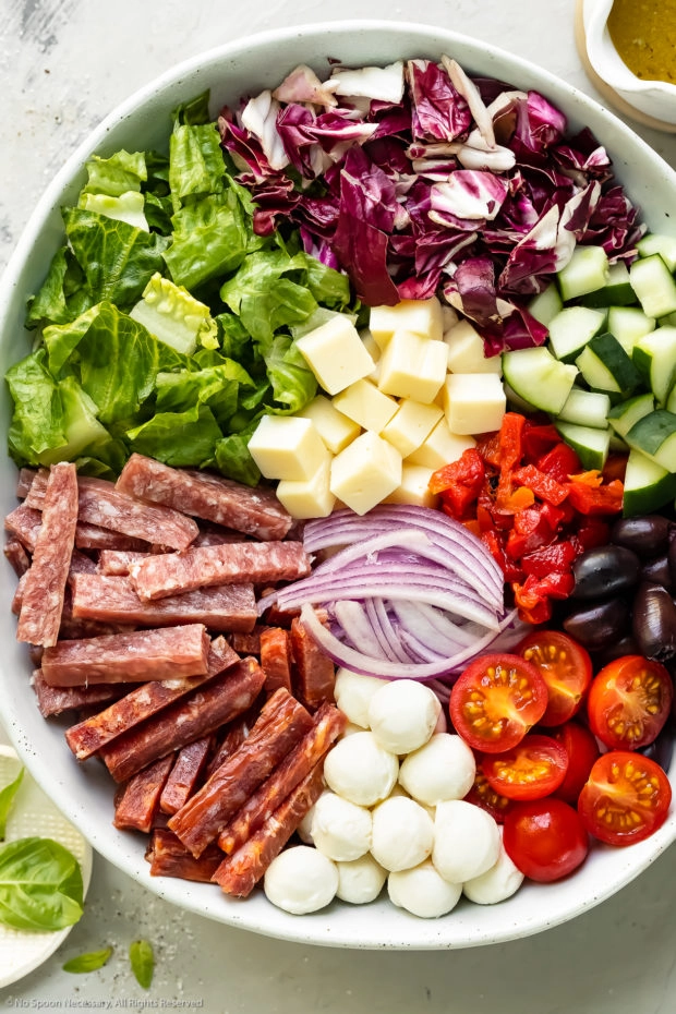 Overhead photo of the Italian chopped salad ingredients neatly arranged in a large serving bowl before being tossed with dressing.