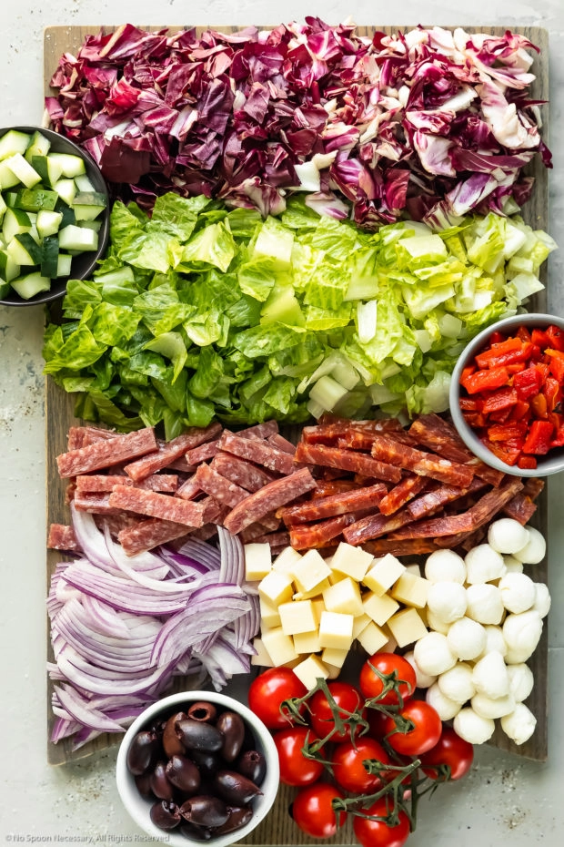 All of the ingredients to make a chopped Italian salad prepped and neatly arranged on a large wood cutting board - photo of all the ingredients needed to make the recipe.