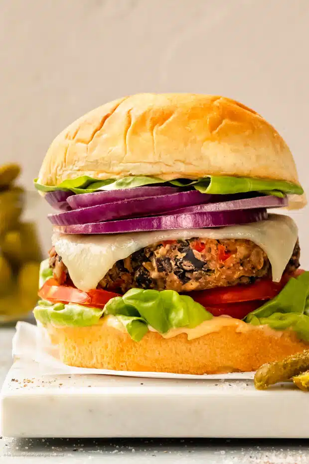 Straight on photo of a veggie burger made with black bean and topped with cheese, lettuce, tomato and onion.