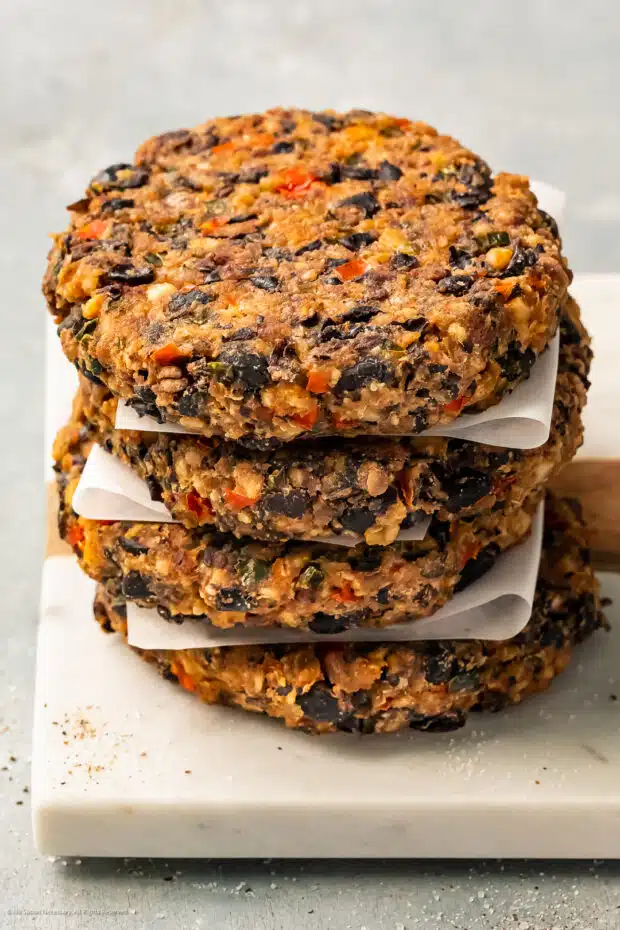 Angled photo of a stack of four cooked veggie bean burger patties on a white plate.