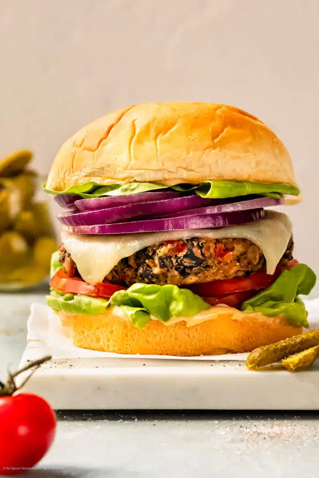 Straight-on photo of a veggie burger with black beans topped with lettuce, tomato, onions, and a pickle.