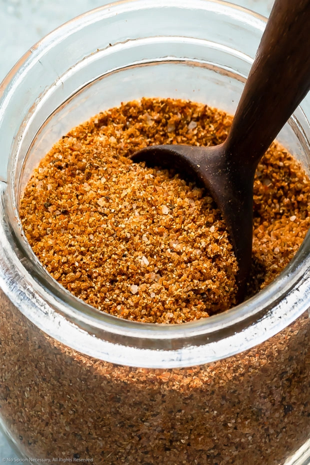 Angled, close-up photo of BBQ Rub in a glass jar with a spoon inserted into the rub.