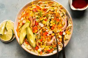 Overhead photo of Mexican slaw garnished with sliced avocado in a white serving bowl.