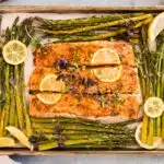 Overhead photo of baked salmon and asparagus with lemon wedges on a sheet pan.