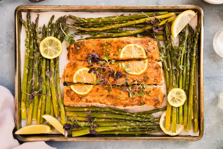 Overhead photo of baked salmon and asparagus with lemon wedges on a sheet pan.