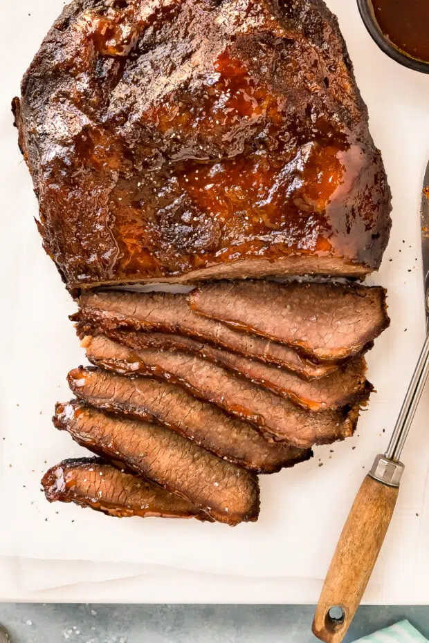 Overhead photo of Slow Cooker Brisket Beef partially sliced on a white cutting board.