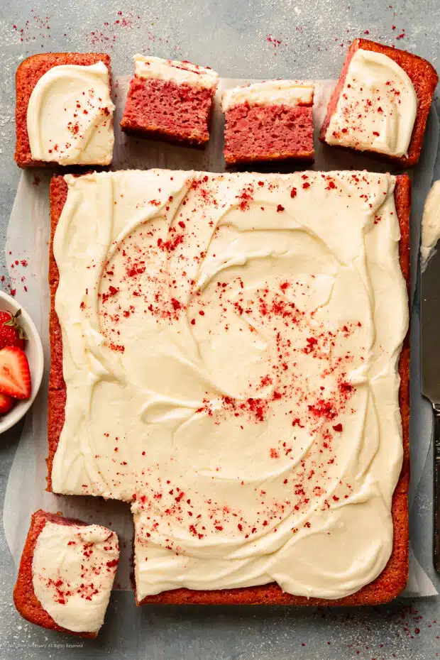 Overhead photo of a strawberry cake with cream cheese frosting cut into individual servings.