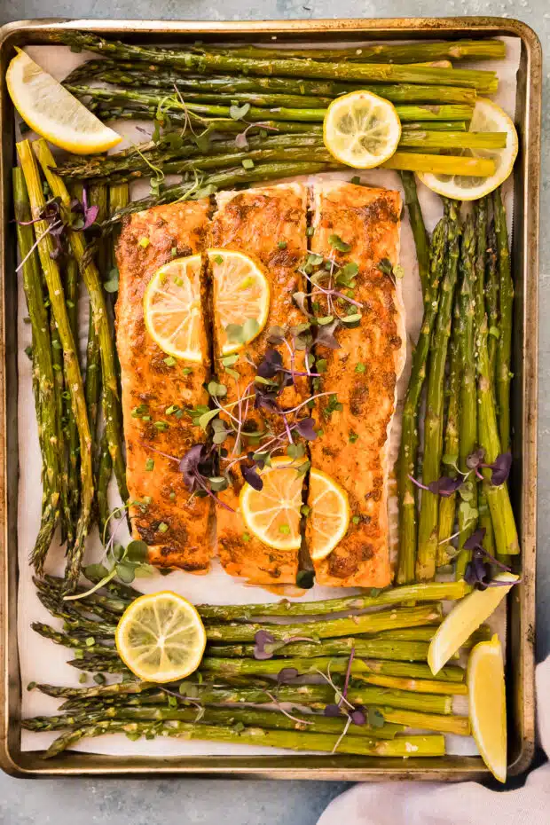 Overhead photo of baked asparagus and salmon with lemon on a sheet pan.