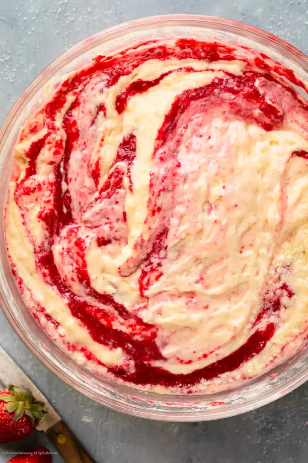 Overhead photo of raw cake batter swirled with fresh strawberry puree.