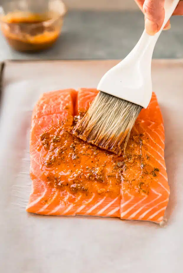 Action photo of lemon marinade being brushed onto a filet of raw salmon.