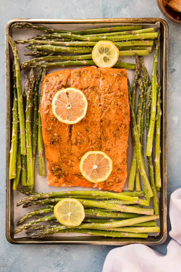 Overhead photo of raw salmon with asparagus and lemon slices on a baking sheet (before roasting).