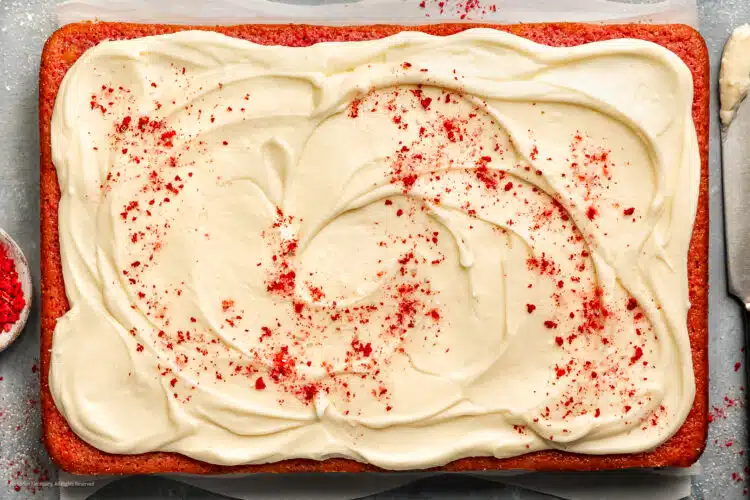 Overhead photo of a baked strawberry sheet cake topped with cream cheese frosting and crushed dried strawberries.