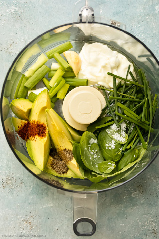 Overhead photo of a food processor bowl filled with the ingredients in green goddess dressing with avocado - before processing.