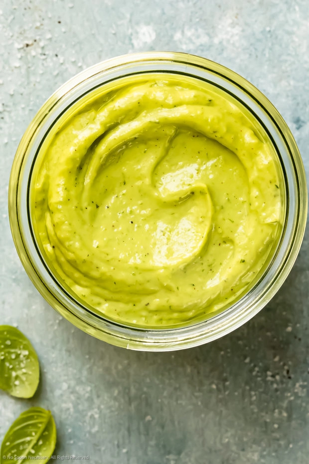 Overhead photo of Avocado Green Goddess Dressing in a glass jar with fresh basil leaves next to the jar. 